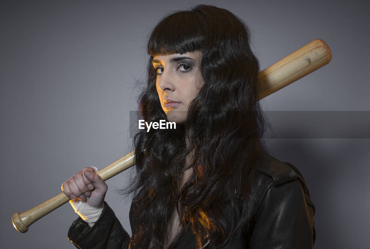 Portrait of young female model holding baseball bat against gray background