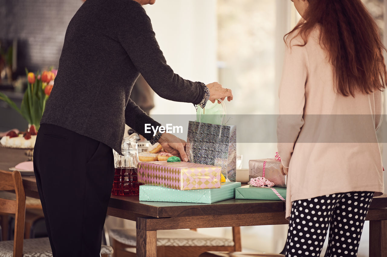 Grandmother and granddaughter arranging gift boxes on table at home