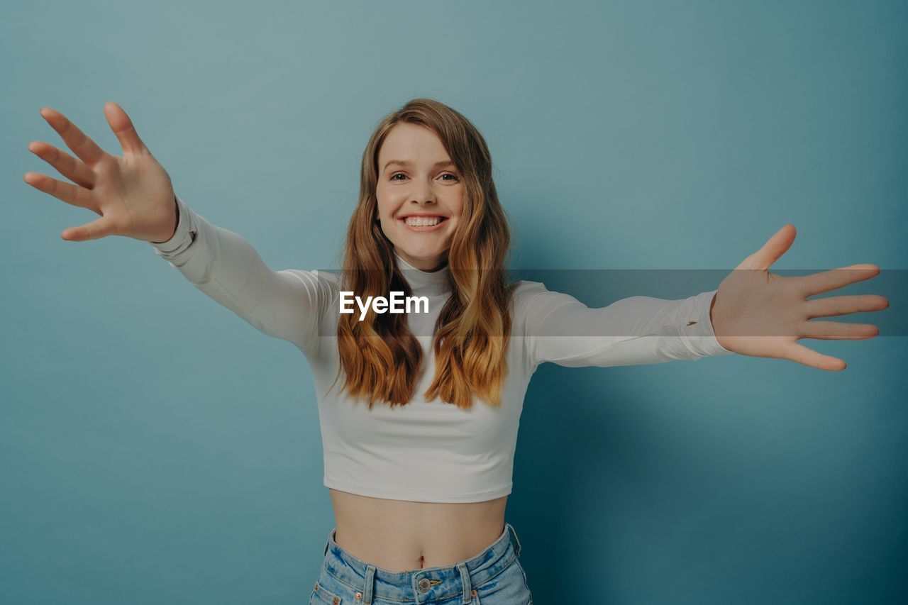 portrait of young woman with arms raised standing against sky
