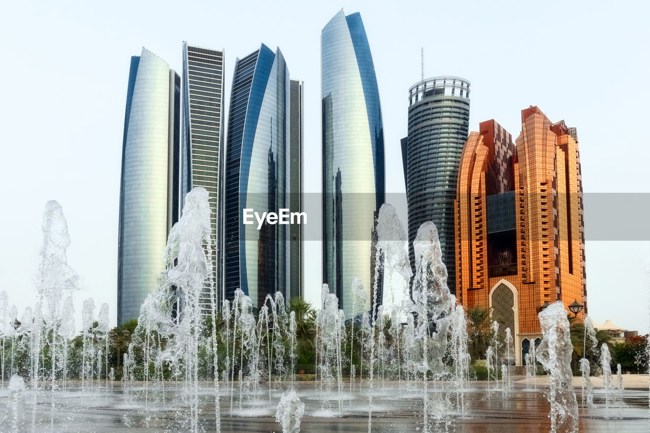 Fountain in front of modern buildings against clear sky