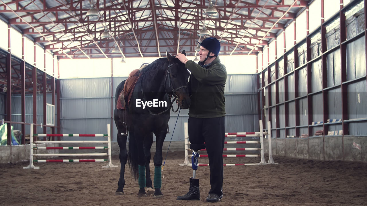 A disabled man jockey strokes a muzzle of a thoroughbred man has prosthesis instead of his right leg