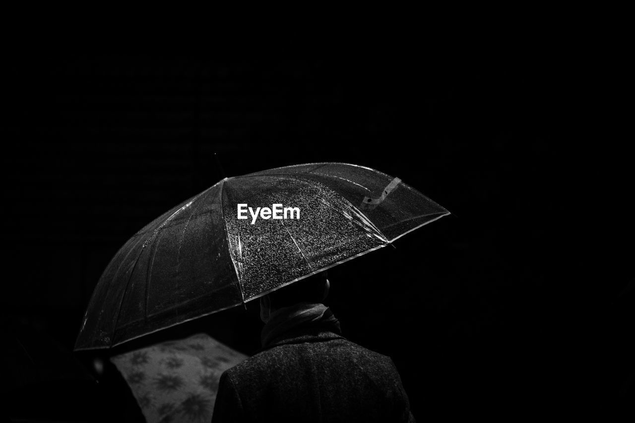 Rear view of man holding umbrella against black background