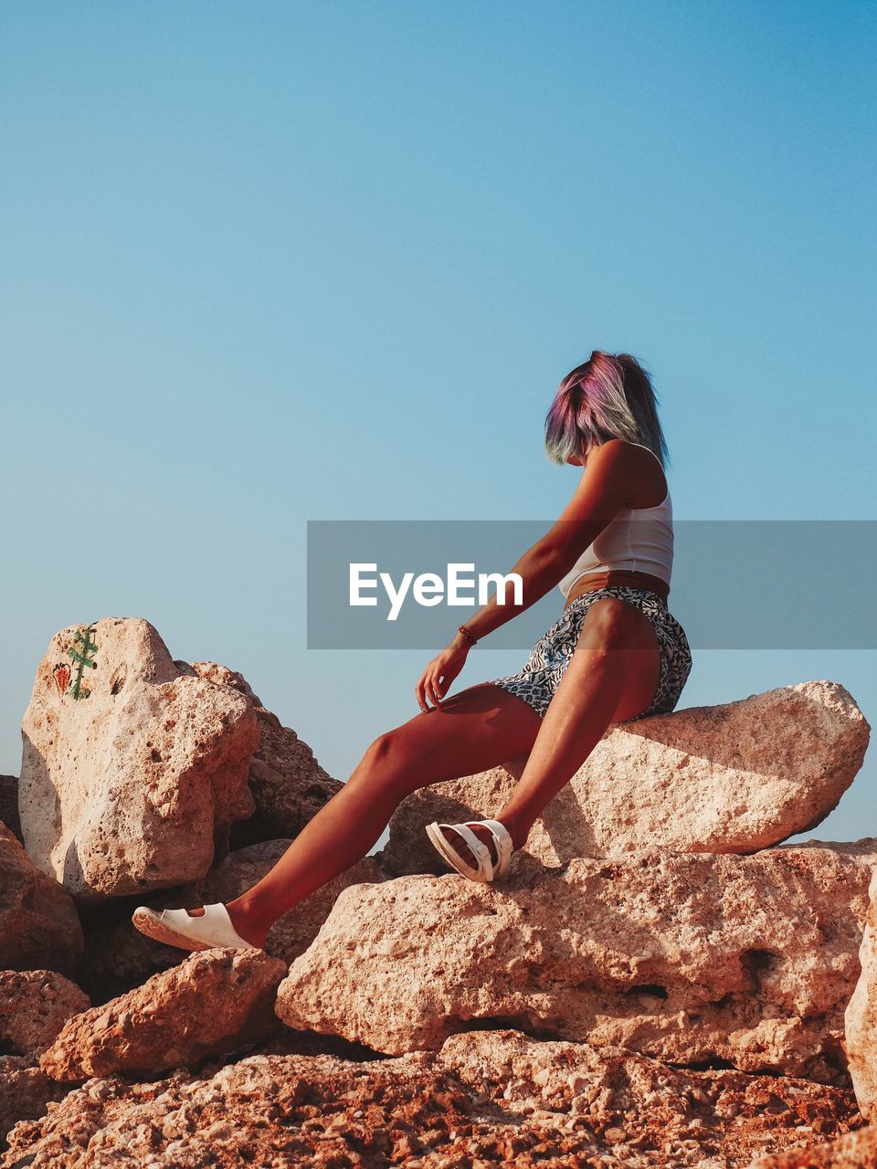 SIDE VIEW OF WOMAN ON ROCK AGAINST SKY