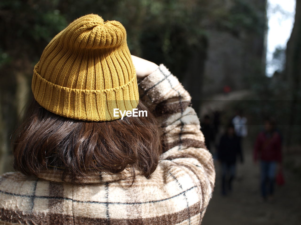 Rear view of woman with short brown hair wearing yellow knit hat standing at park