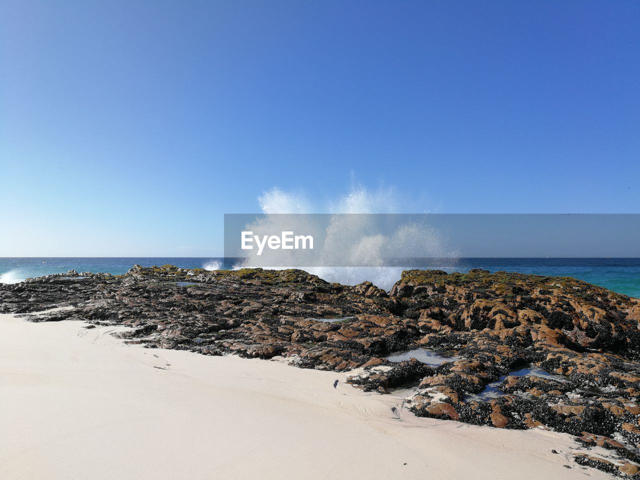 Panoramic view of waves on beach against clear blue sky