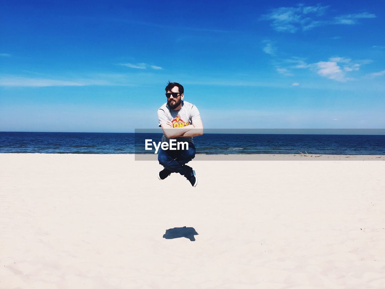 Full length of man sitting in mid-air over beach against sky