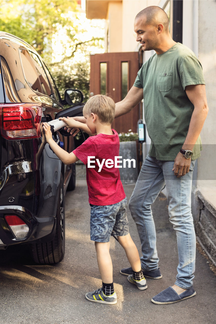 Father and boy charging electric car by house