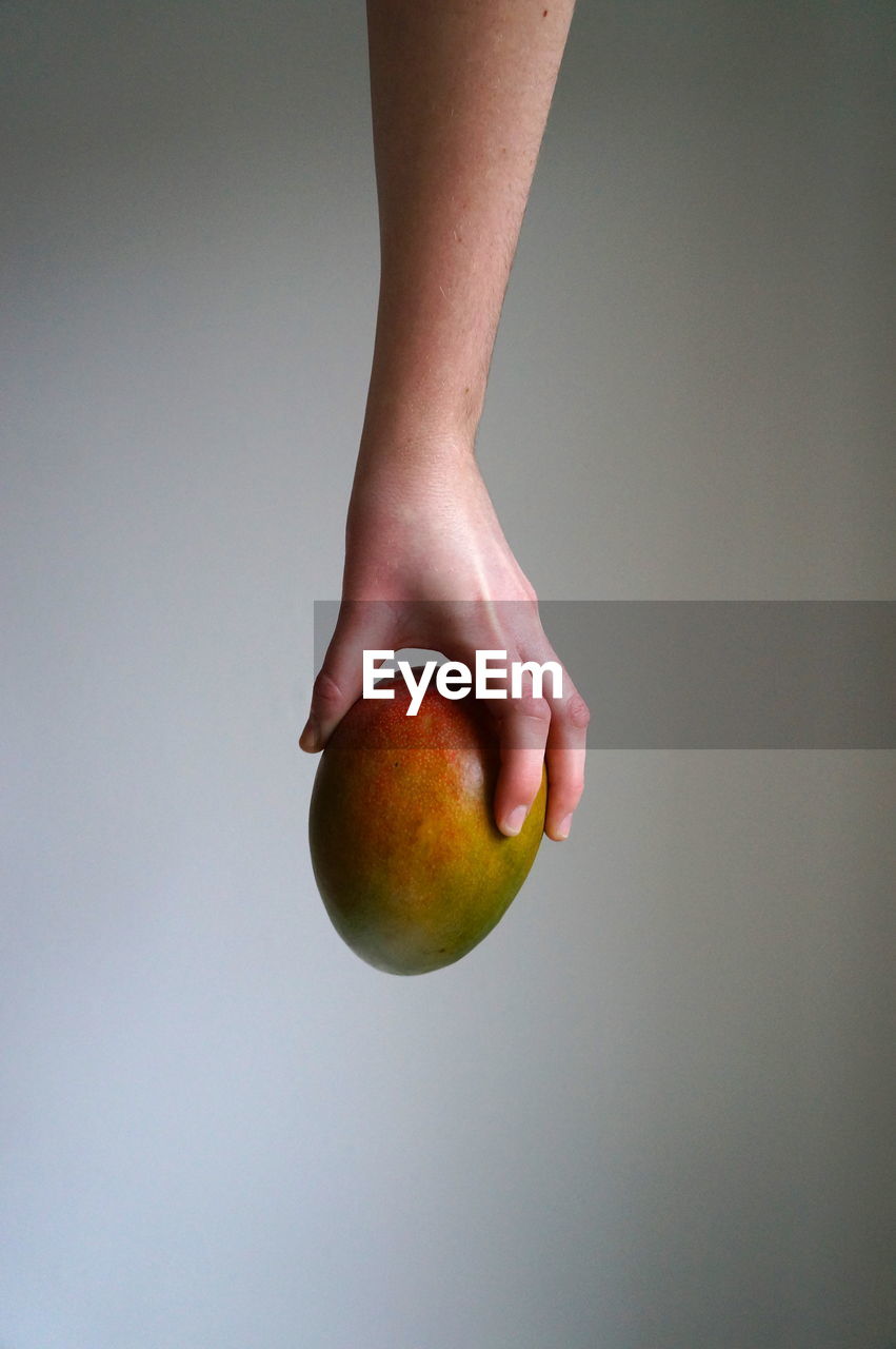 Cropped hand holding mango against wall