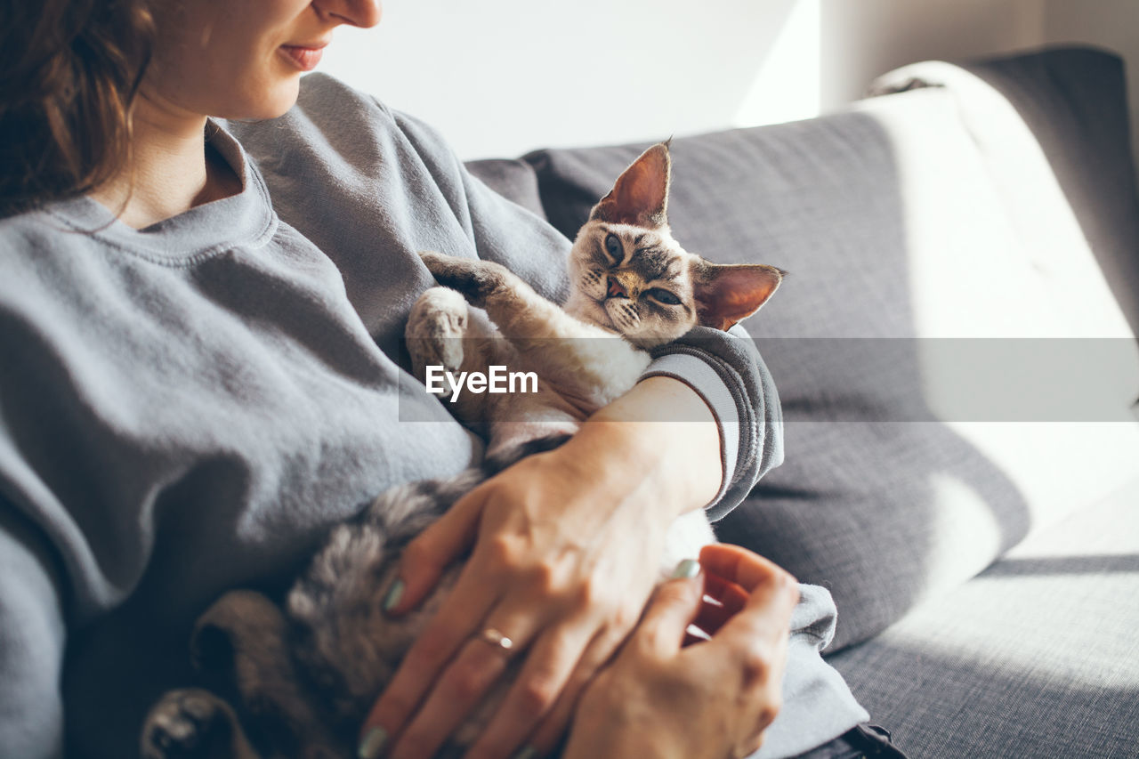 Midsection of woman with cat relaxing on sofa at home