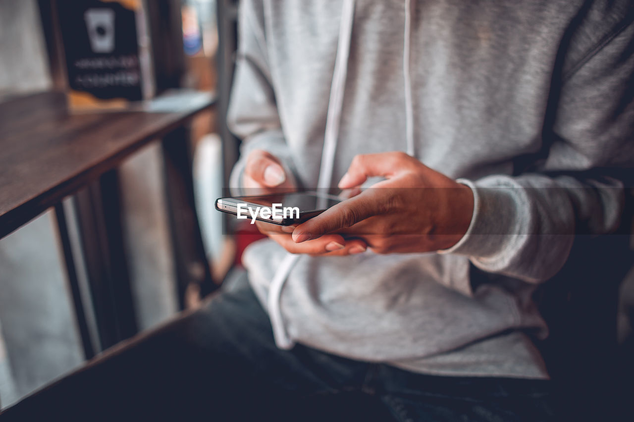 MIDSECTION OF MAN USING MOBILE PHONE IN LAPTOP