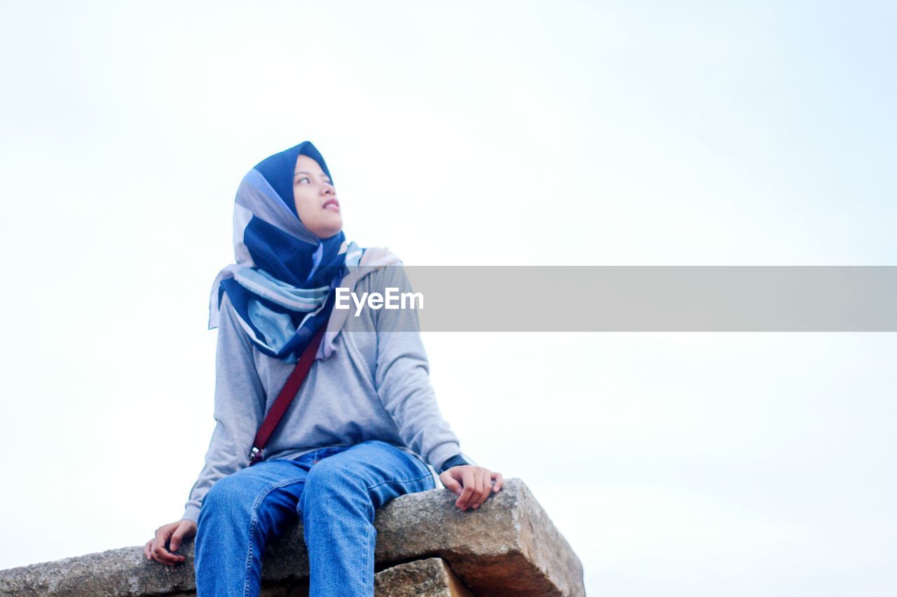 Low angle view of woman looking away against clear sky