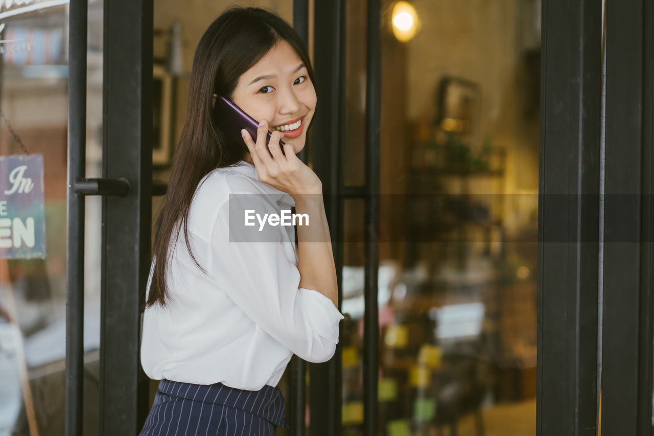 Portrait of smiling young woman talking on phone outside cafe