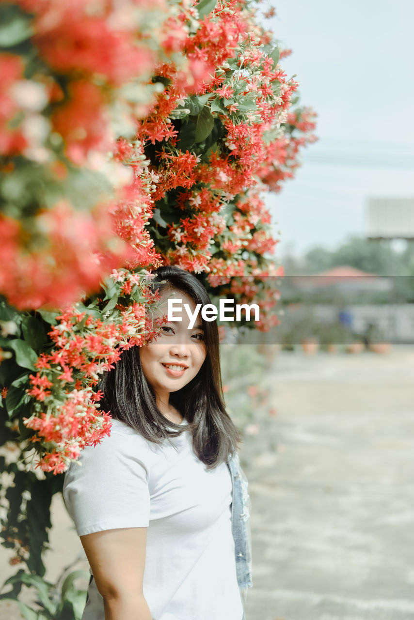 Portrait of smiling young woman standing by flowering plants