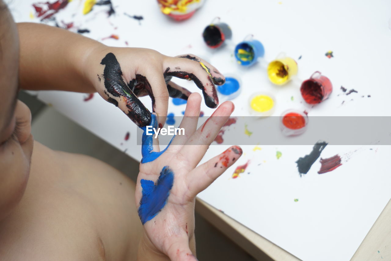 HIGH ANGLE VIEW OF PERSON HAND ON MULTI COLORED TABLE