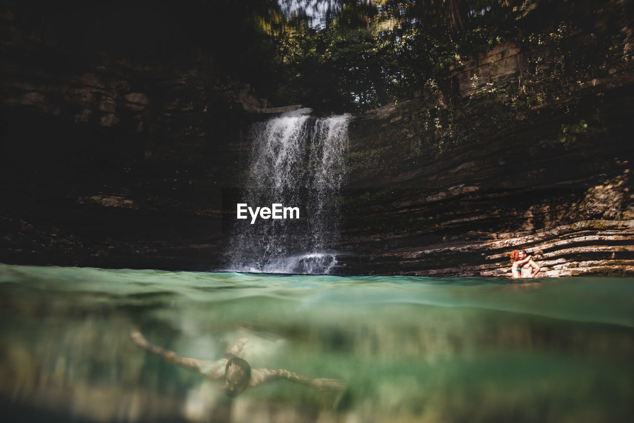 Man swimming in river against waterfall