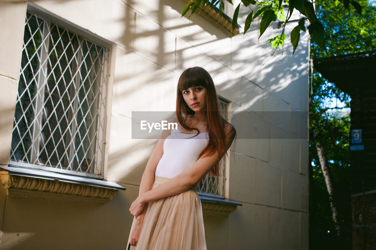 Portrait of young woman standing against building