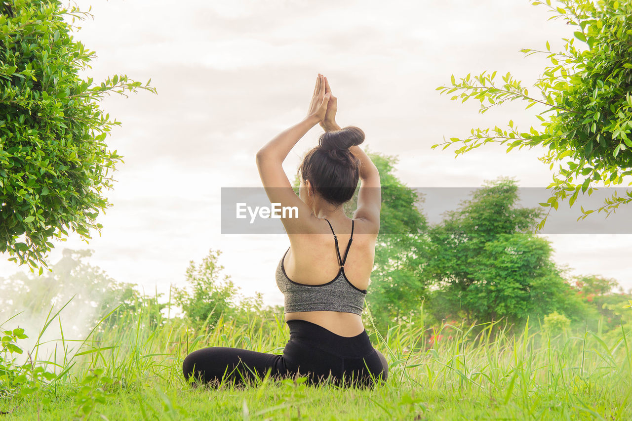 Woman doing yoga while sitting on grassy field