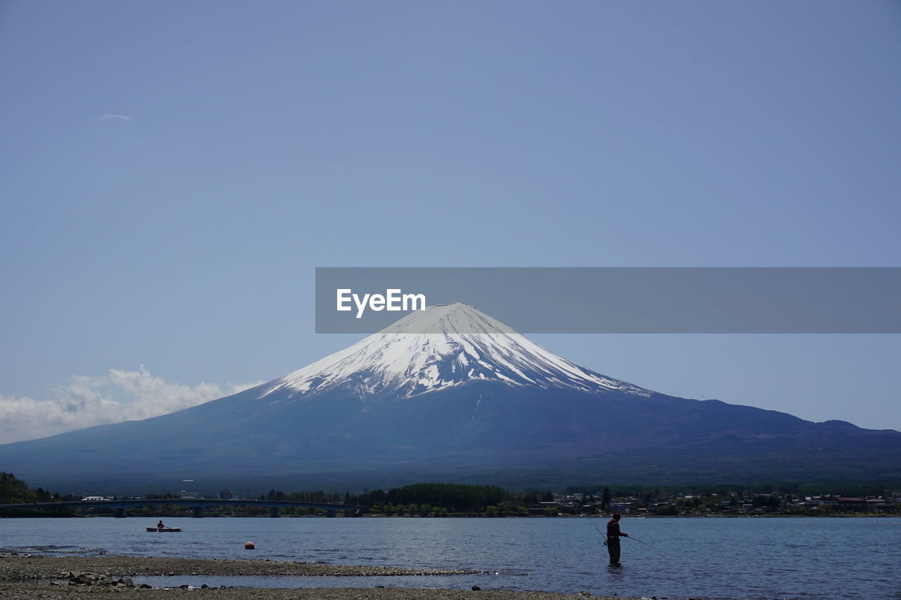 Person fishing in lake against snowcapped mountain