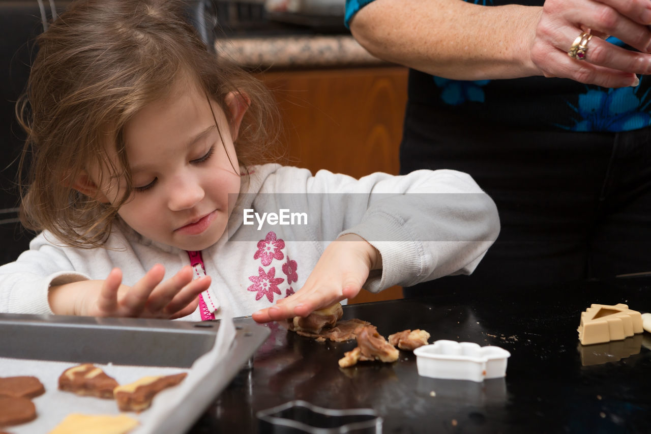 Girl preparing cookie with mother on kitchen island at home