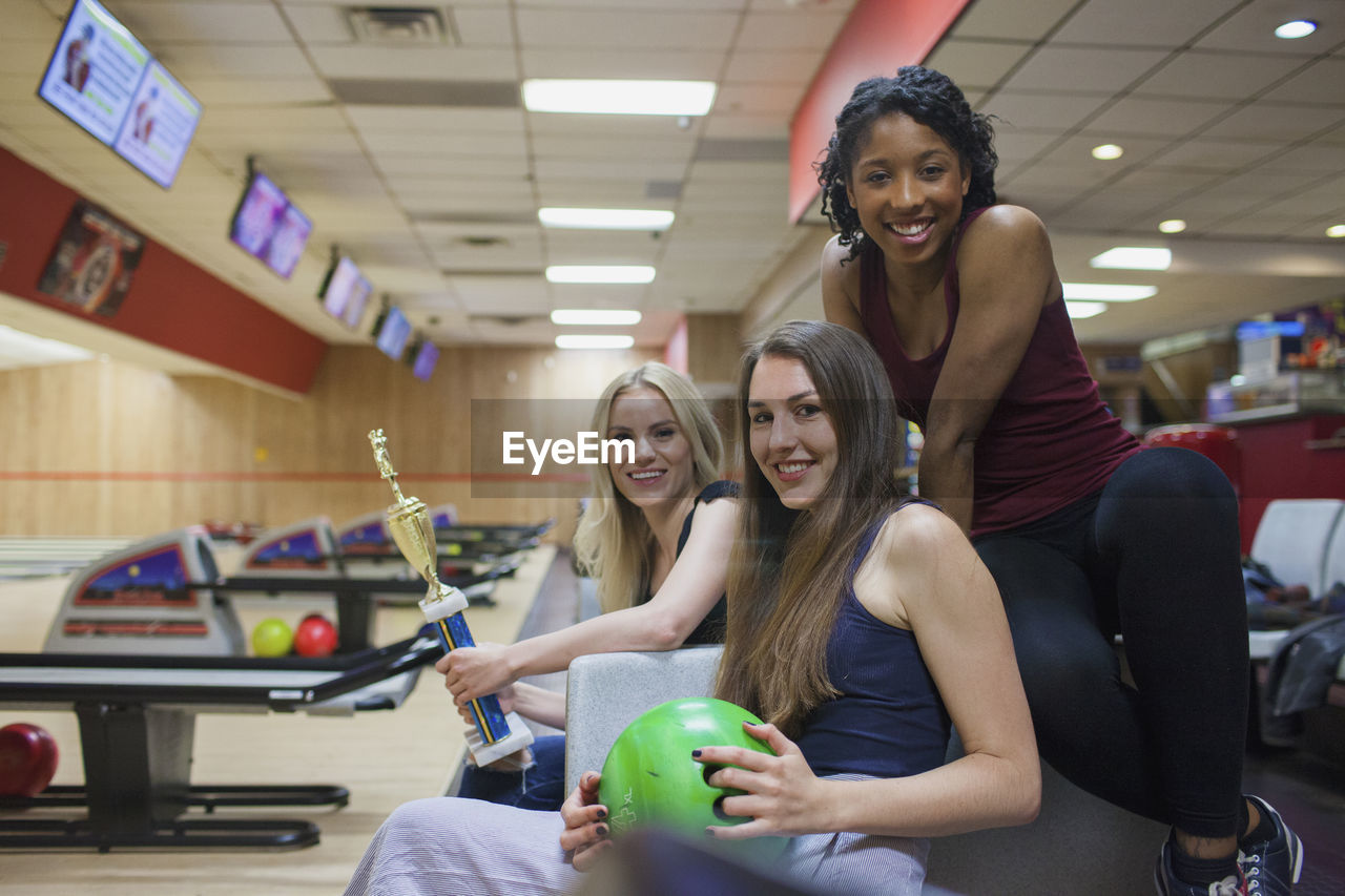 Three young women with a trophy in a bowling alley.