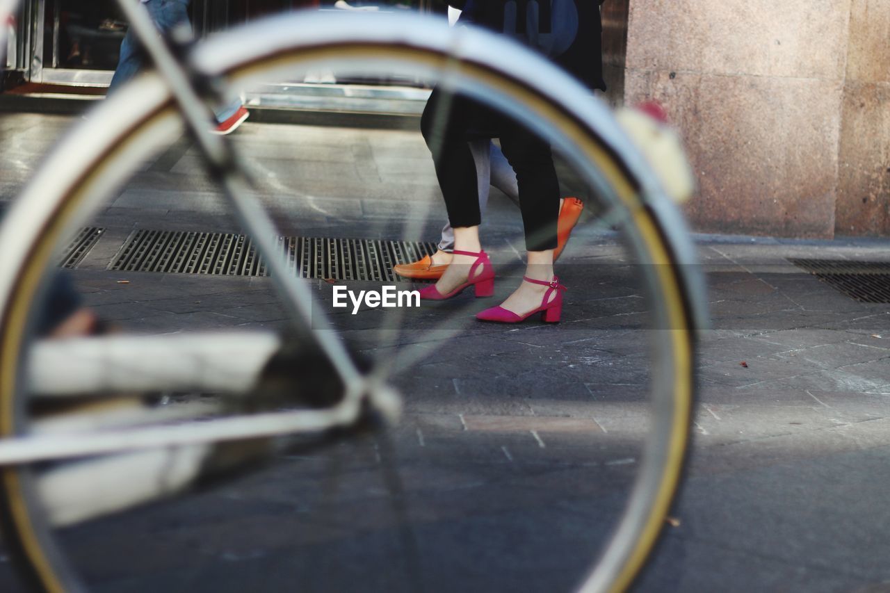 Close-up of bicycle wheel with low section of women in background