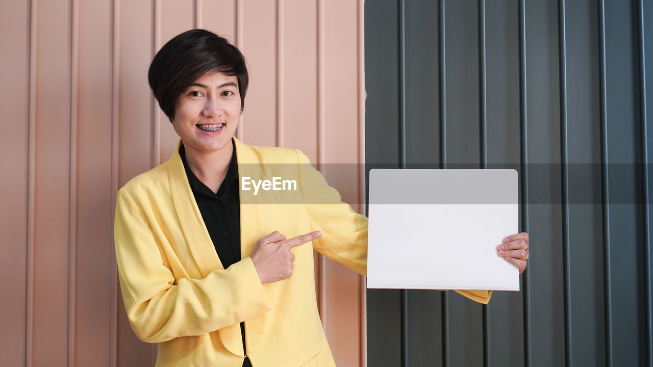 Working asian smart woman in yellow suit holding white copy space card in luxury interior background