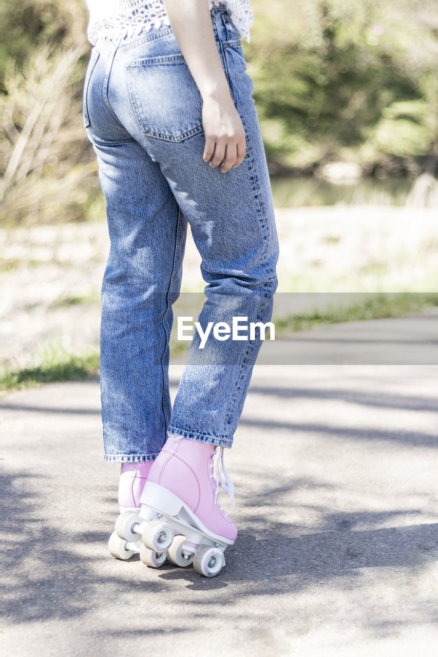 Woman's legs in jeans and pink roller skates in a park