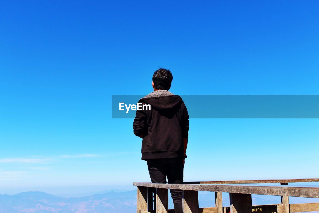 Rear view of man standing against clear blue sky