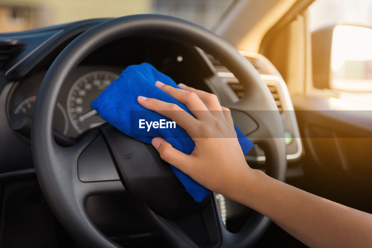 Cropped hand of woman cleaning car steering wheel