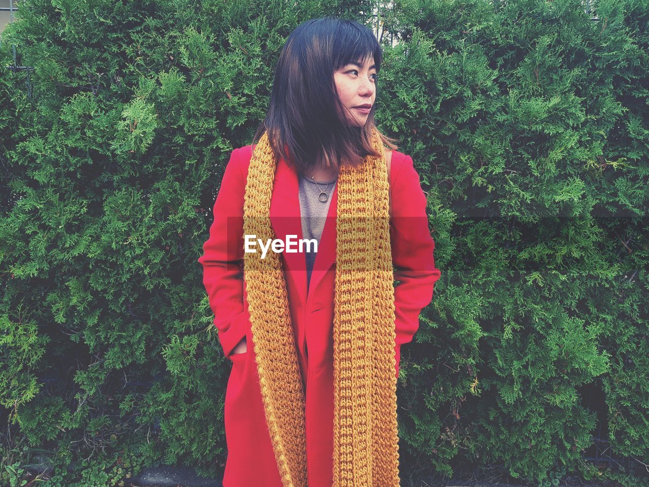 Woman wearing red overcoat while standing by plants