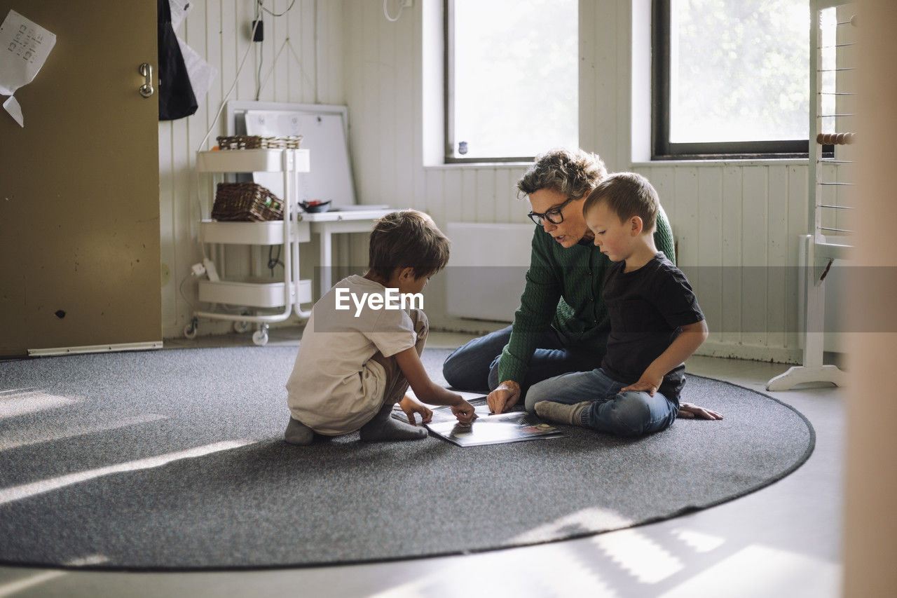 Preschool kids studying with senior female teacher while sitting on carpet in classroom at school