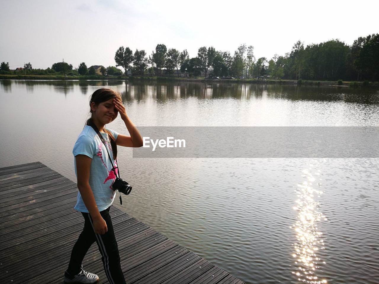 Girl with camera standing on pier over lake against sky