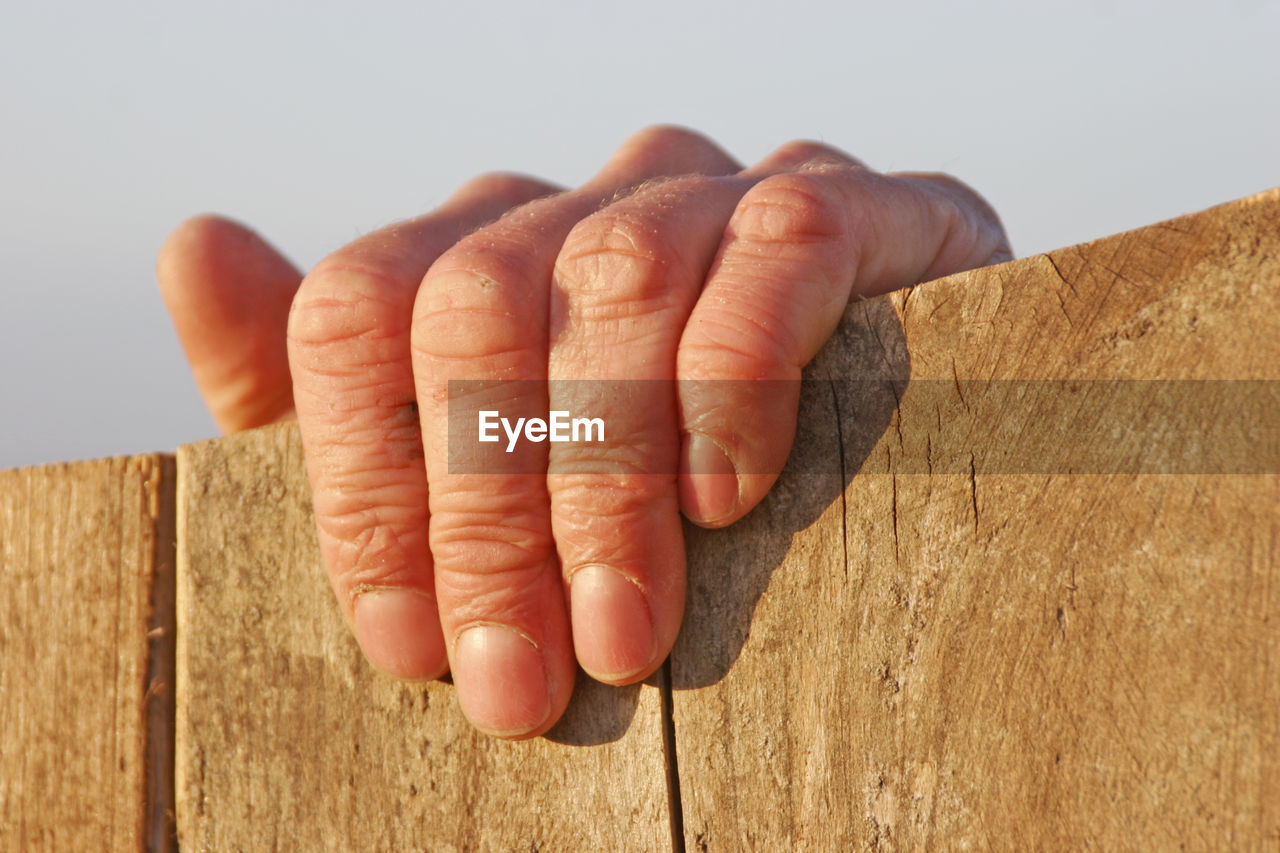 Close-up of human hand gripping onto wooden surface