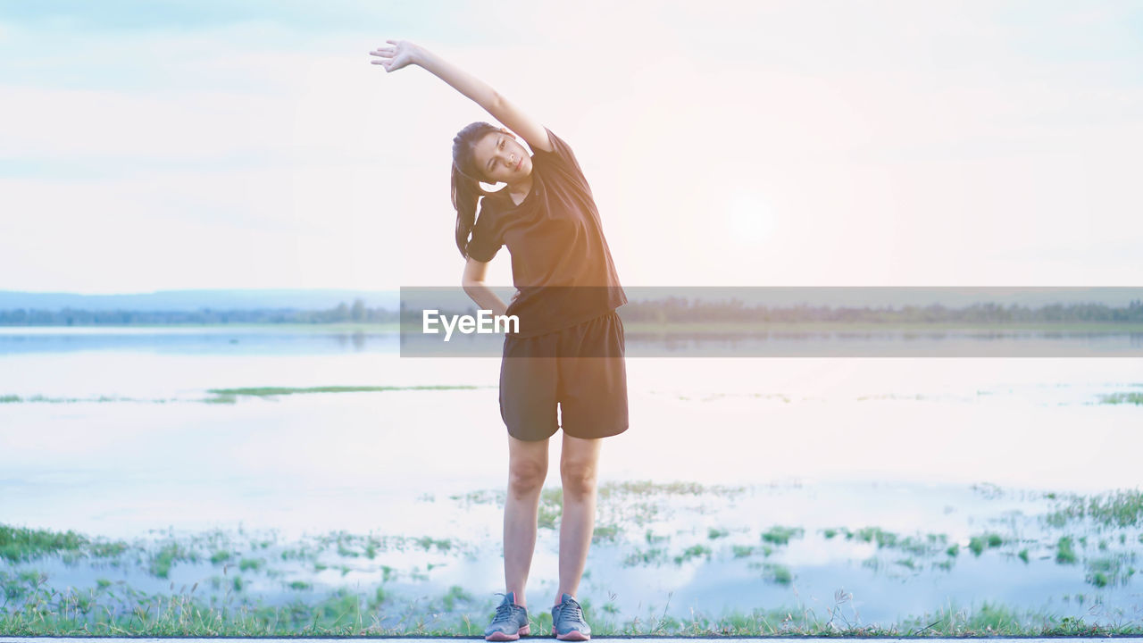 Woman exercising against lake at sunset