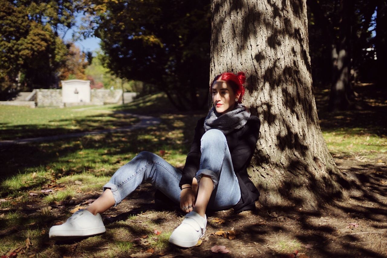 Woman sitting against tree trunk at field