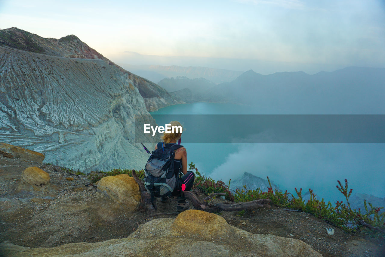 Woman looking at view while sitting on mountain against sky