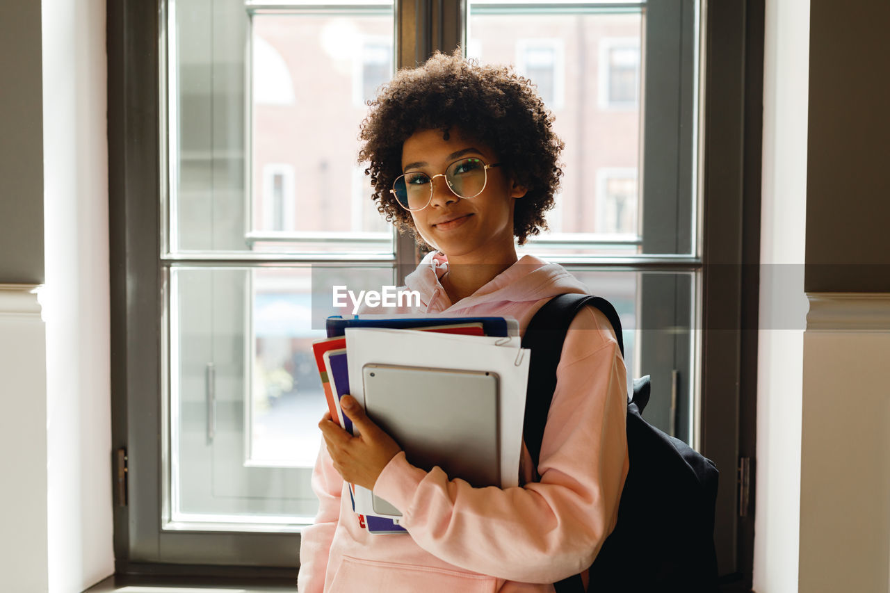 Teenage girl wearing eyeglasses holding books at home