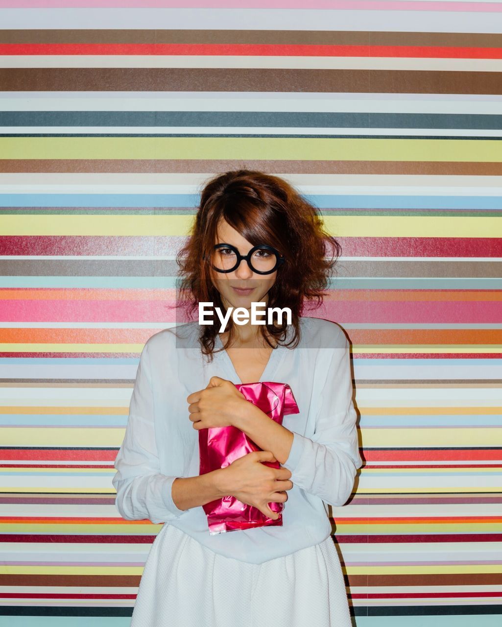 Portrait of young woman holding bag while standing against colorful wall