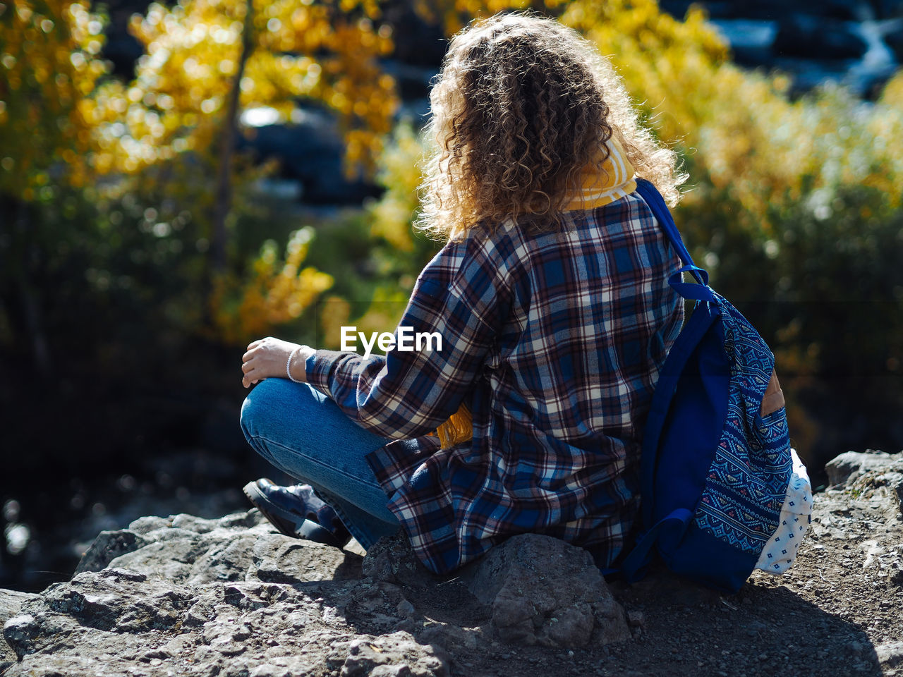 Young curly woman traveller in yoga pose doin meditation on a hill in autumn forest