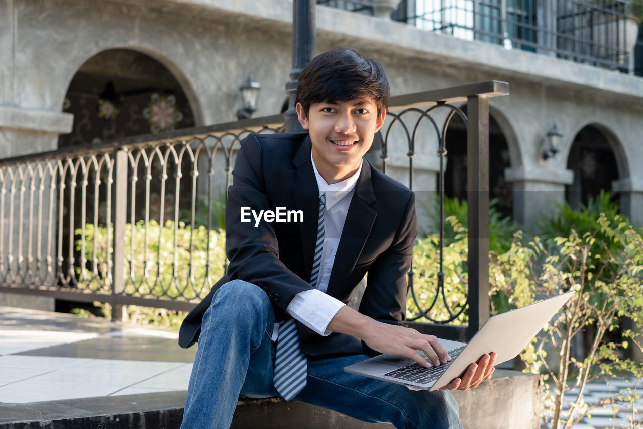 portrait of young man using laptop while sitting in city