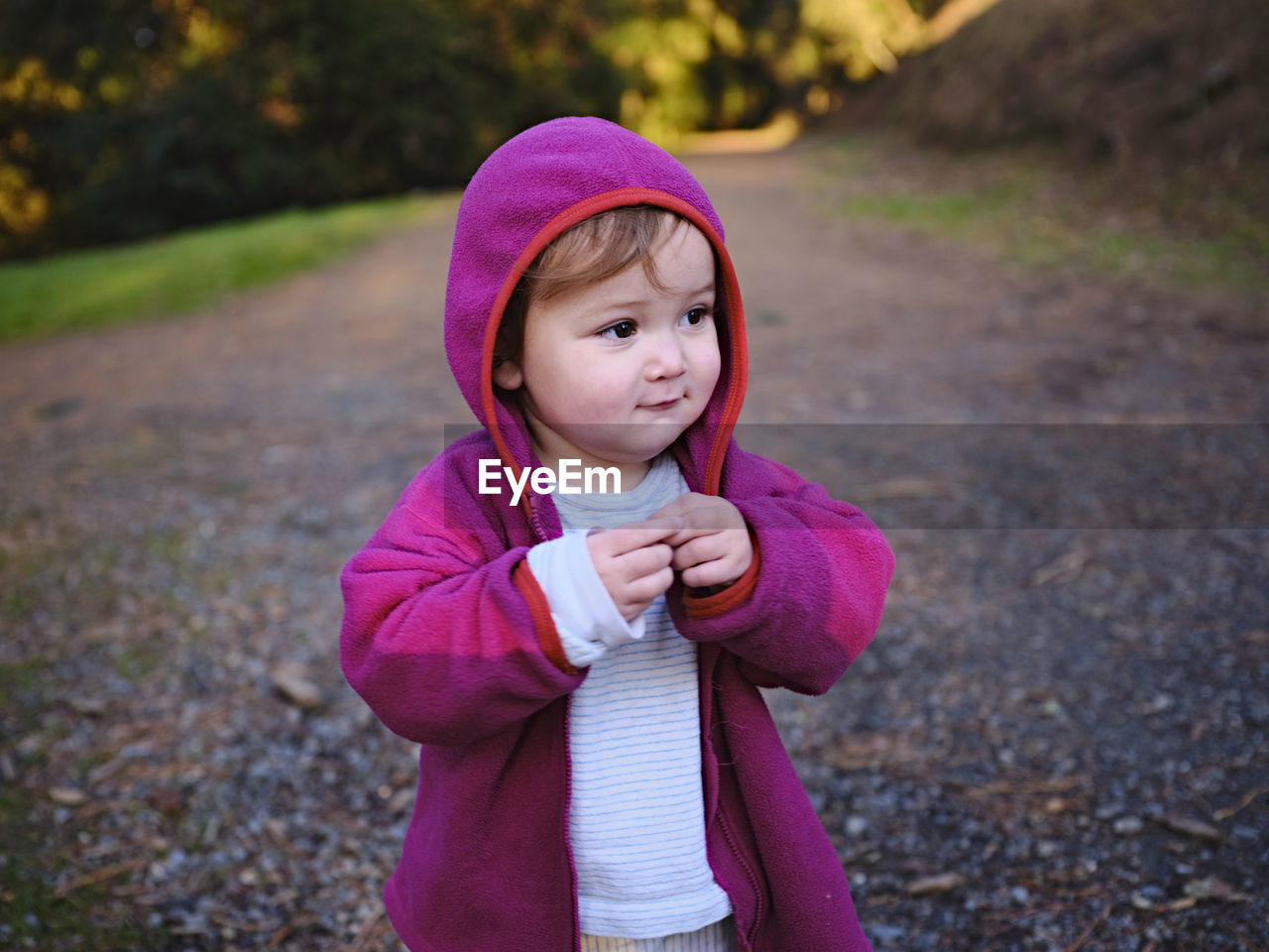 A toddler grins and looks away from the camera at the start of a trail