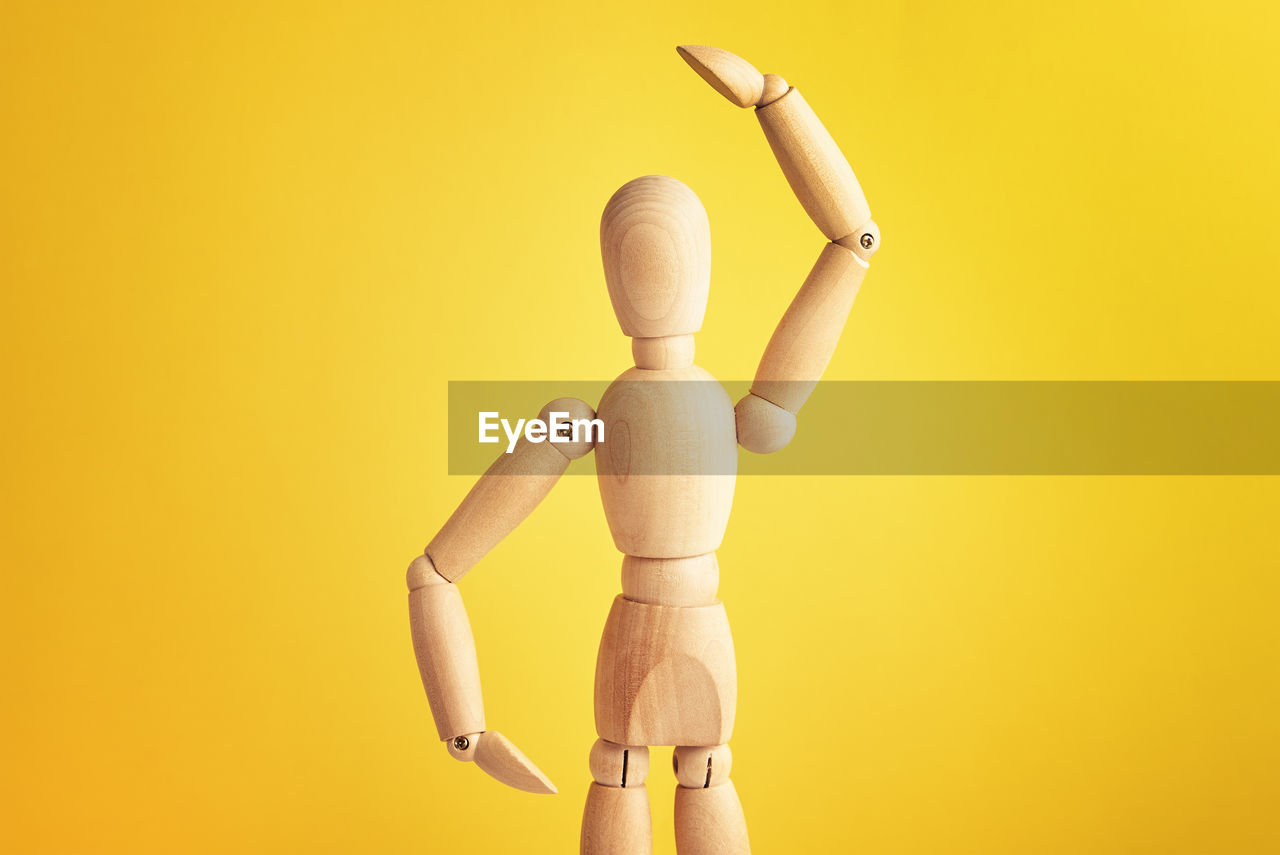 Wooden doll with gesture on yellow background. mannequin shows gesture. figure of wooden human