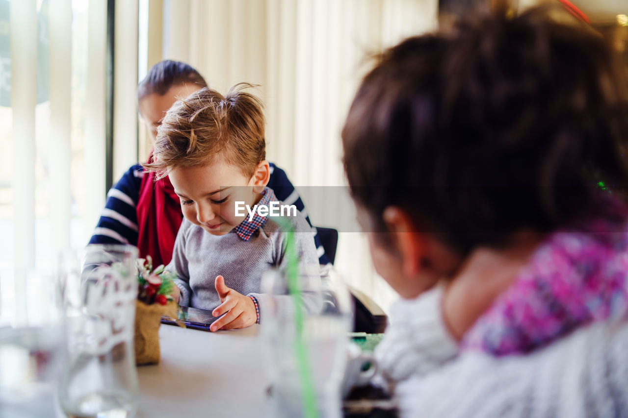 Mother sitting with son using smart phone on table at home