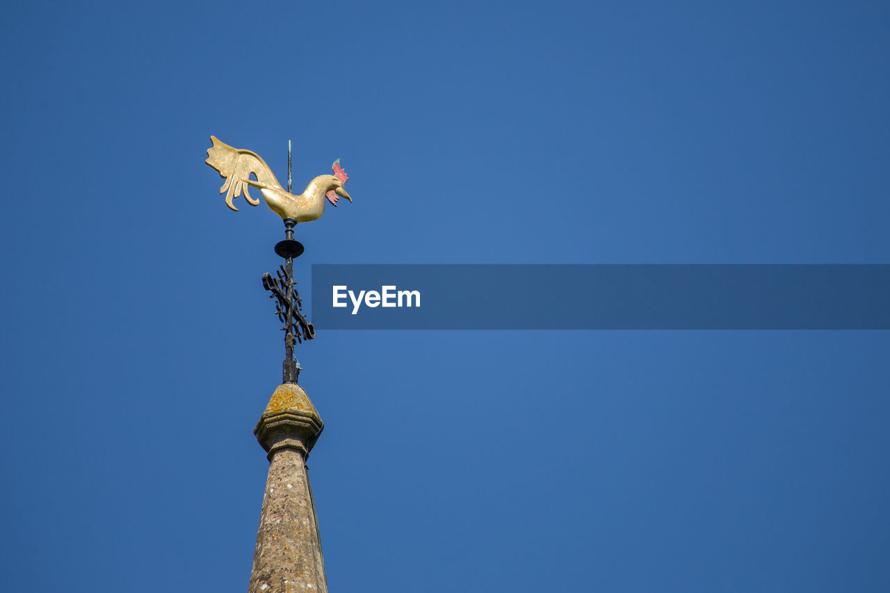 Low angle view of weather vane against clear blue sky