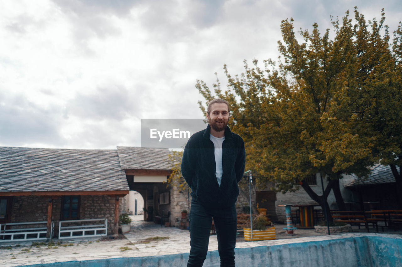 Portrait of smiling man standing by tree against sky