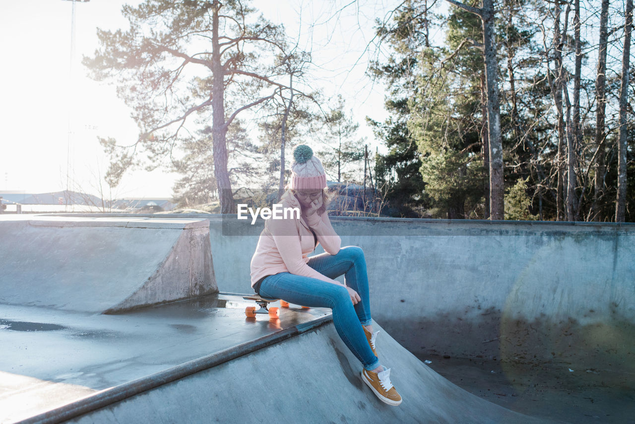 Woman sitting on her skateboard in a skatepark thinking in the sun