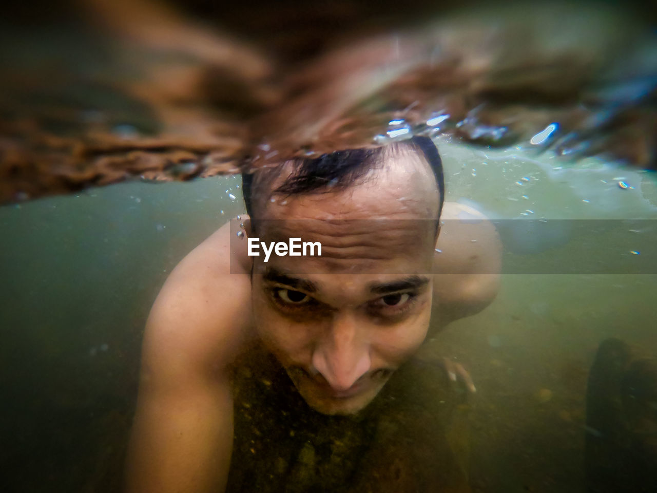 Man swimming in natural waterfall underwater shot from low angle