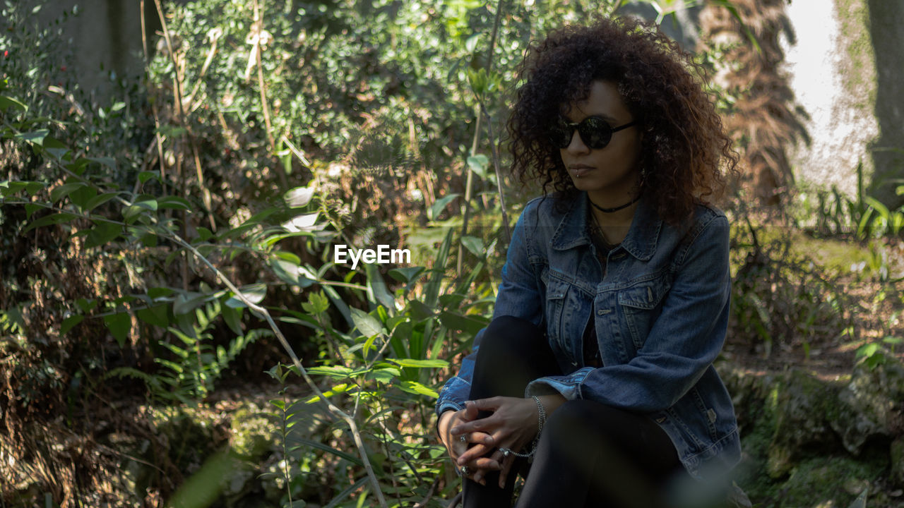 Young woman with curly hair sitting on field amidst plants at park