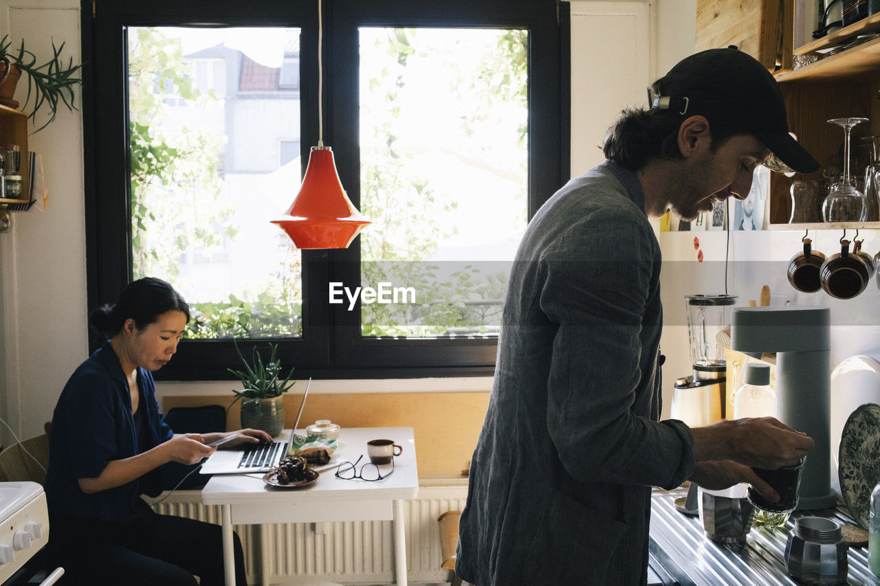 Male architect preparing coffee while female colleague using smart phone in home office