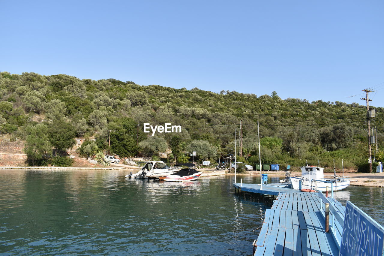 water, nautical vessel, transportation, tree, sky, nature, clear sky, mode of transportation, plant, sea, land, blue, travel, no people, boat, vehicle, vacation, bay, day, travel destinations, scenics - nature, beauty in nature, tranquility, beach, moored, sunny, boating, ship, outdoors, marina, tourism, holiday, environment, landscape, trip, tranquil scene, architecture, dock, idyllic, waterfront, sunlight, harbor, non-urban scene, pier, coast, tropical climate, watercraft, forest, coastline, summer